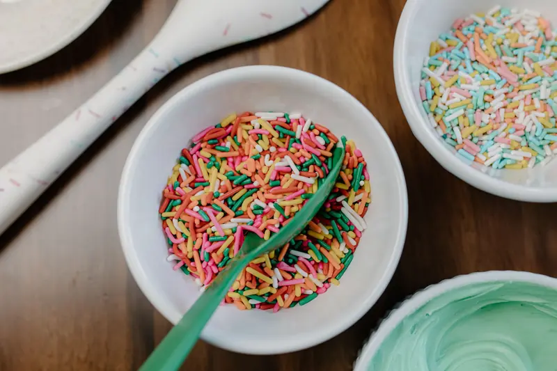 Top-down view of colorful sprinkles in bowls on wooden surface, perfect for baking decoration
