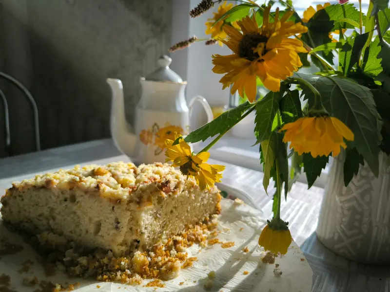 A delicious homemade crumb cake accompanied by vibrant sunflowers and a teapot on a sunlit table