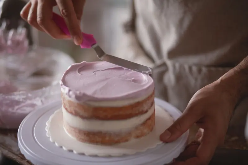 Close-up of a baker skillfully frosting a naked cake with pastel icing