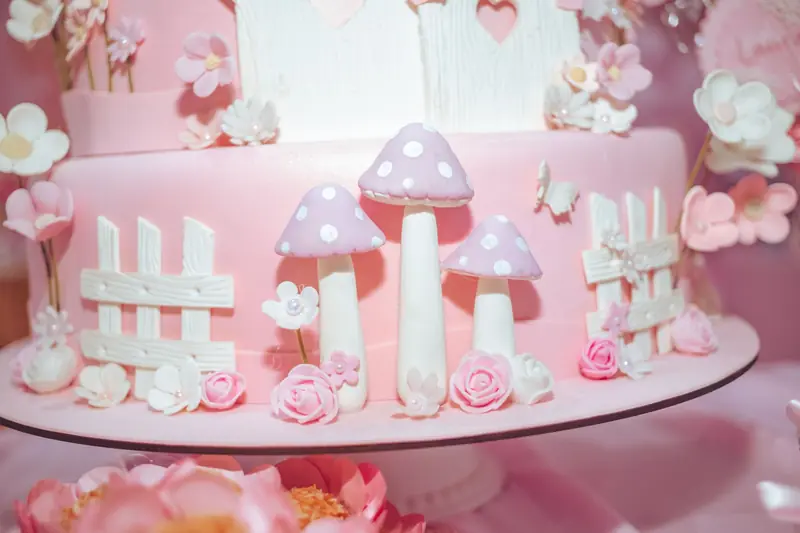 Charming pink cake adorned with fondant mushrooms and flowers, perfect for whimsical celebrations