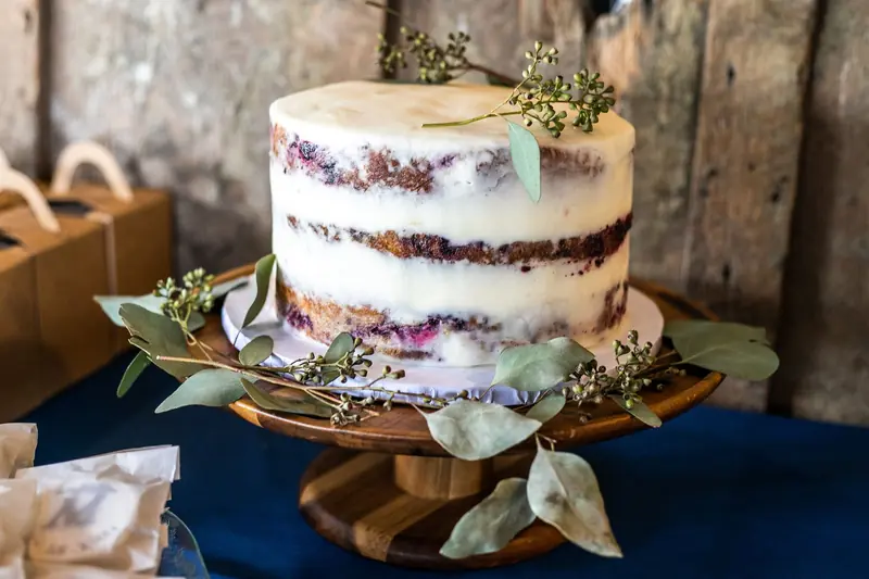 A rustic naked cake adorned with fresh greenery on a wooden cake stand, perfect for weddings or celebrations