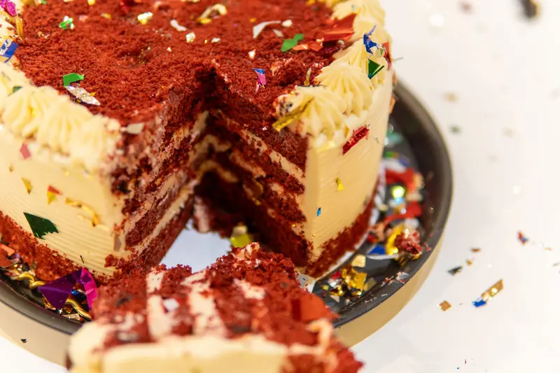 Red velvet cake slice with cream cheese frosting and colorful confetti for party celebration