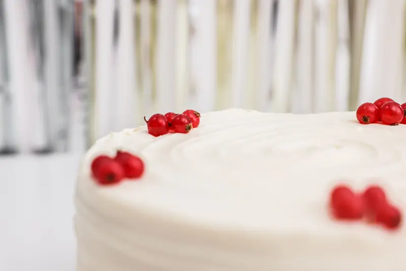 Close-up of a white frosted cake topped with vibrant red currants