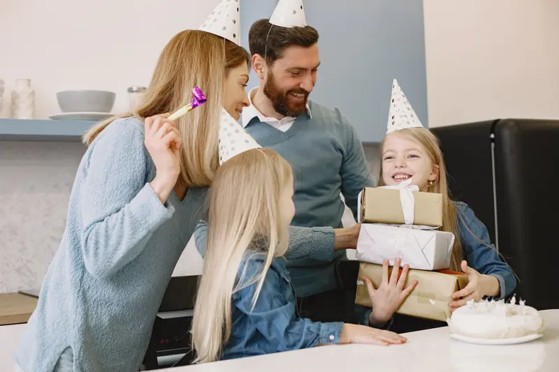 A joyful family celebration with gifts, cake, and party hats in a cozy indoor setting