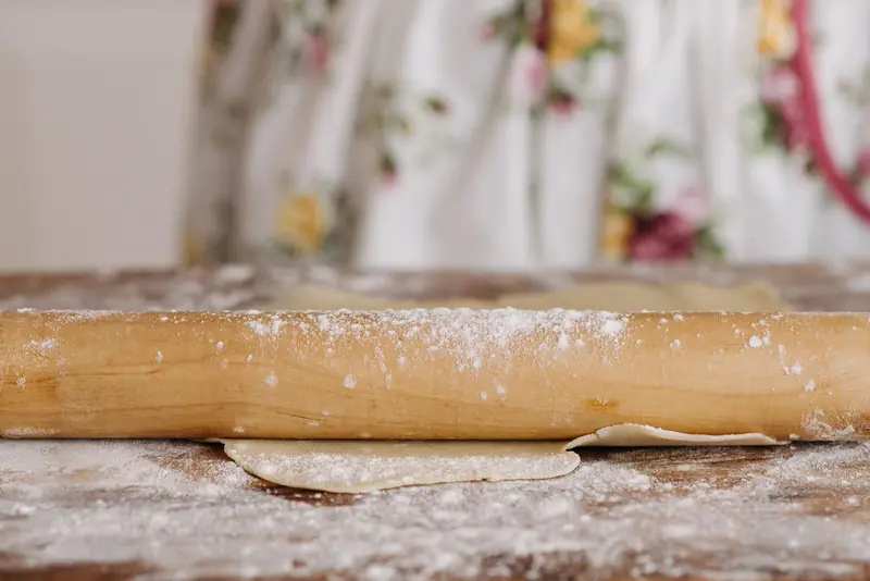 A wooden rolling pin rolling out dough on a flour-dusted surface, perfect for baking themes