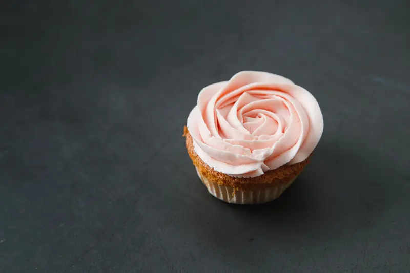 Delicate cupcake with rose-shaped buttercream frosting on a dark surface, perfect for dessert and bakery themes