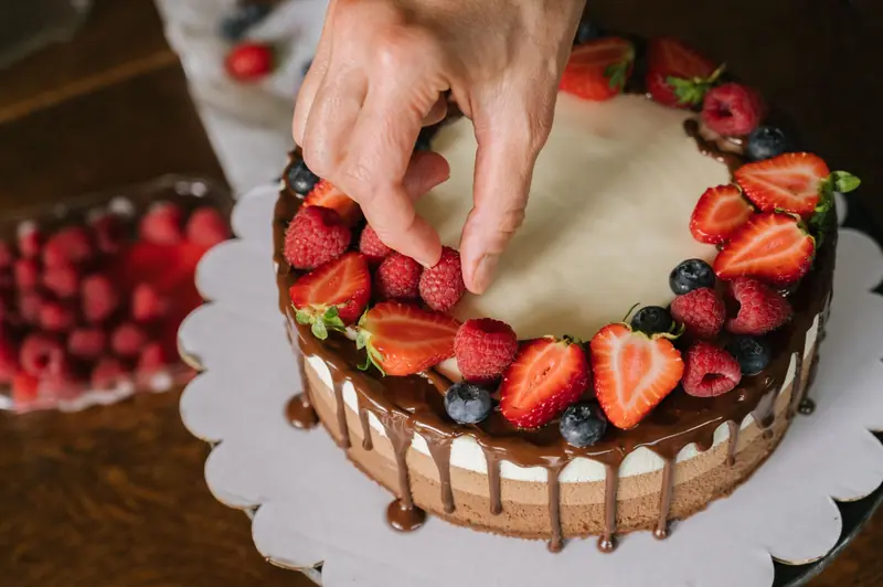 Hand placing fresh berries on a chocolate-covered cake, creating a delicious dessert