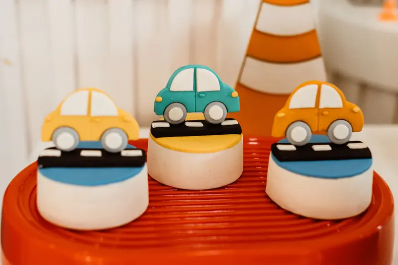 Vibrant car-themed fondant cake toppers on a red surface, ideal for children's parties
