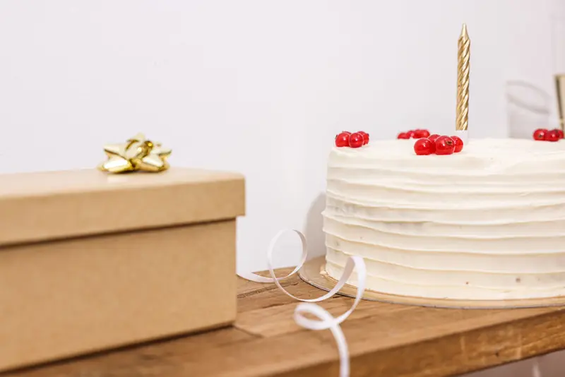 A beautifully decorated birthday cake with a golden candle beside a gift box, creating a festive celebration atmosphere