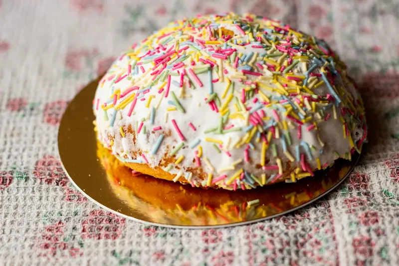 A close-up of a cake covered in white icing and colorful sprinkles on a patterned tablecloth