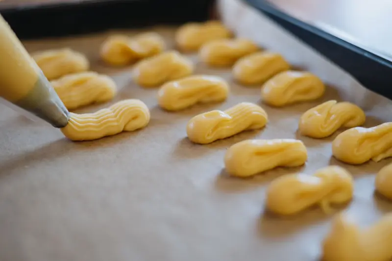 Pastry bag piping dough onto a baking sheet for eclairs preparation. Close-up food photography