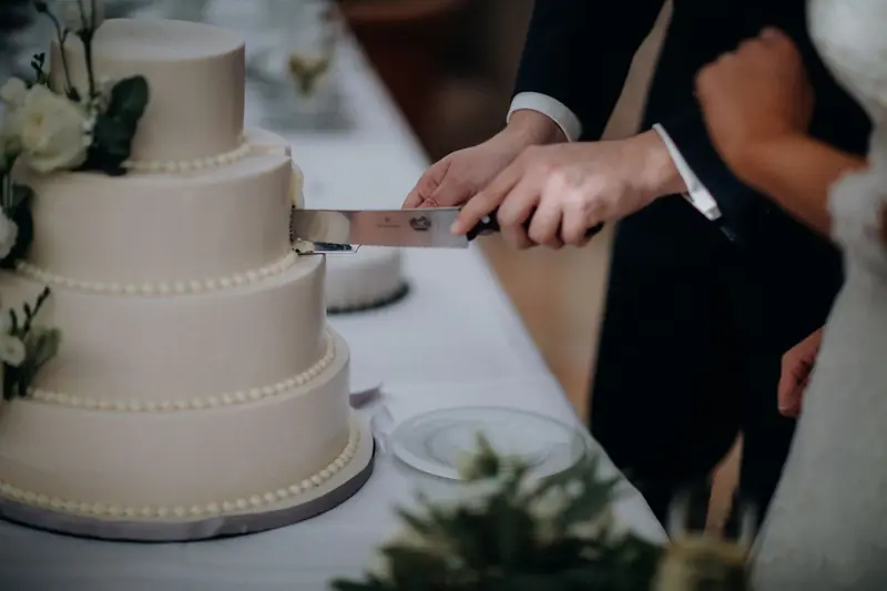 Close-up of a couple cutting a tiered wedding cake with flowers